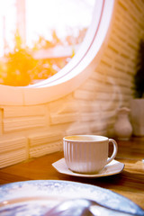 Hot coffee in white cup near window. Coffee cup in coffee shop.