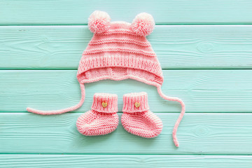 Knitted pink footwear and hat for baby on mint green wooden background top view