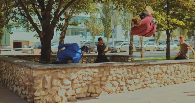 Parkour on a city street. Cute guys doing somersaults and jumping in the park, extreme street sport.
