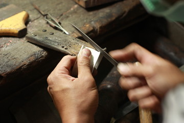 hands and tools of a professional silversmith working on a piece in his traditional workshop,...