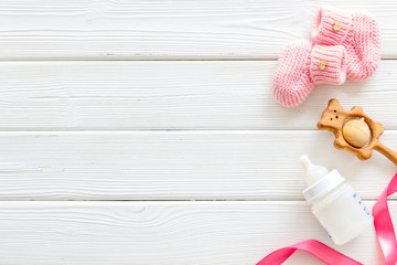 Booties for newborn girl with rattle and bottle on white wooden background top view mock up