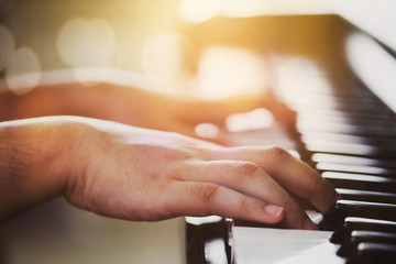 Close up of a man hands playing on piano keys with window light and Bokeh effected. Music background with copy space.
