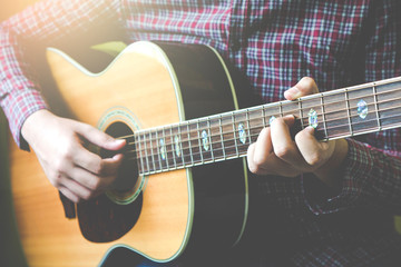 Young guitar player plays acoustic guitar in front of yellow background
