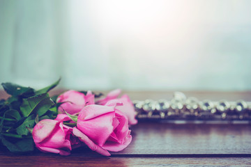 close up of pink roses and flute on wooden table  against window light, copy space