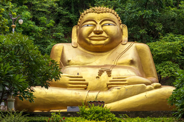 Large golden statue of Sangkhachai Buddha amid forest.