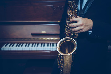 Close up of a man hand hold and playing saxophone over piano with light effected, music poster cover background, copy space for your text or design