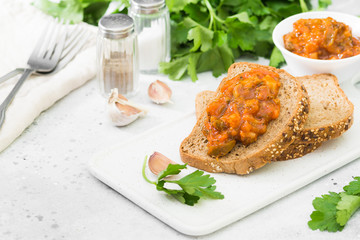 Bread with vegetable caviar on a white tray on a light gray table