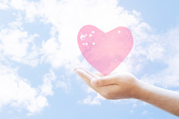 young man hands with pink heart against white clouds  blue sky background
