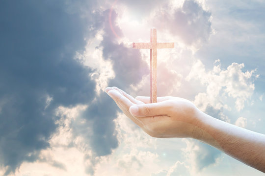 Human hands holding wooden cross against the light from cloudy blue sky, Christian background, image of worship or trust concept