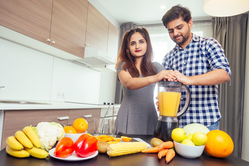 healthy and eco lifestyle.happy indian woman with her husband making smoothie in big kitchen