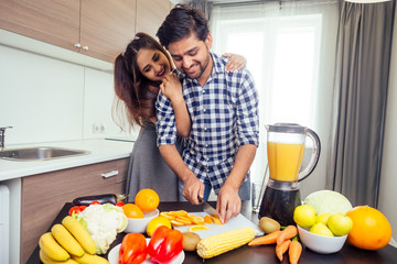 happy indian woman and handsome man mixing fruits for fresh smoothie in bright day light cozy kitchen