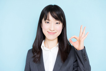 Young business woman showing OK sign against light blue background