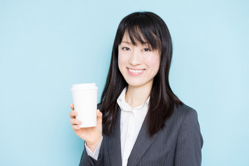 Young business woman holding coffee against light blue background