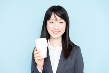Young business woman holding coffee against light blue background
