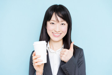 Young business woman drinking coffee against light blue background