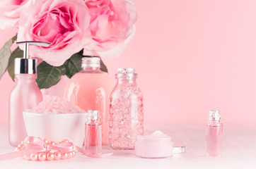 Obraz na płótnie Canvas Cosmetics products for bath, spa - essential oil, bath salt, cream, liquid soap, towel and pink roses in delicate pastel pink bathroom interior, closeup.