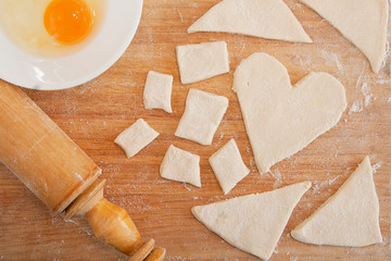 Heart-shaped dough on a cutting board, raw egg, rolling pin, home cooking