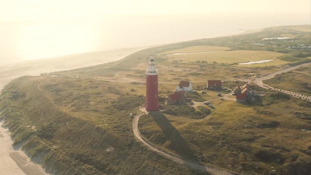 Aerial orbiting shot of the beautiful lighthouse revealing wide sand beach at the Texel island (part of Wadden islands) in The Netherlands, shot in the morning after sunrise