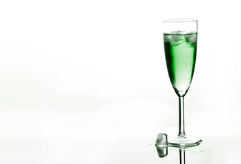 Glass of green champagne with ice on white background