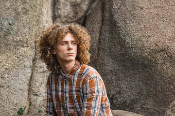 portrait of a young curly-haired guy among the stones on the street. student and young traveler concept