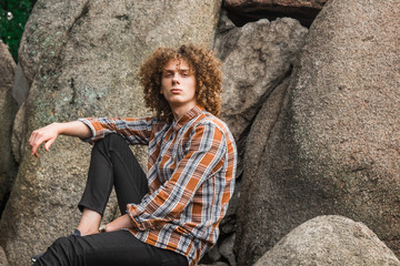 portrait of a young curly-haired guy among the stones on the street. student and young traveler concept