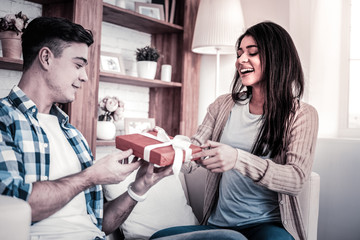 Openly laughing woman presenting her gift to boyfriend nearby
