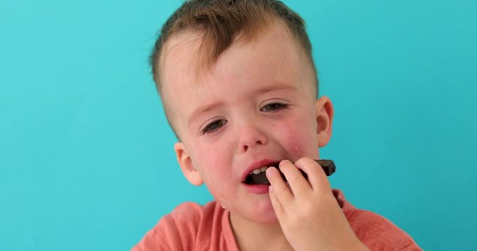 Little boy is upset eating chocolate. The young child is visibly mad or sad on blue background