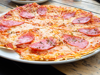 sliced whole salami pizza on a wooden table, selective focus