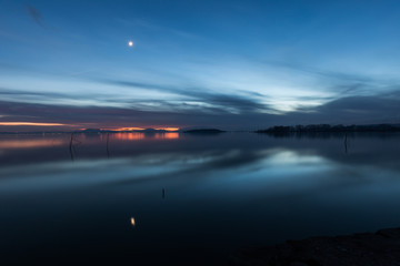 Moon above a lake with its reflection on the Trasimeno lake surface at dusk