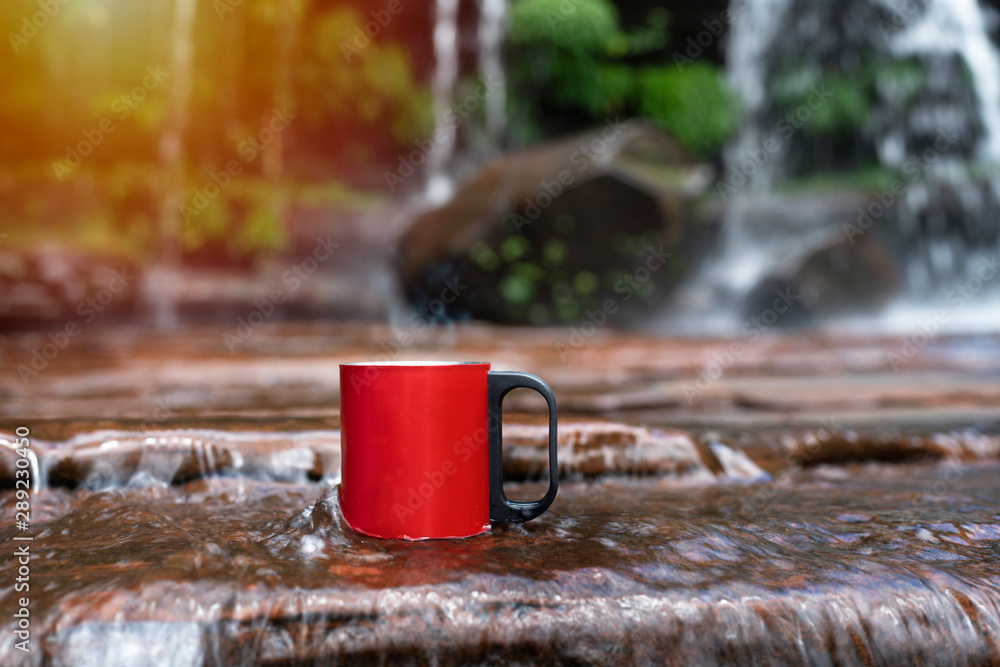 Wall mural red cup of coffee with waterfall nature background