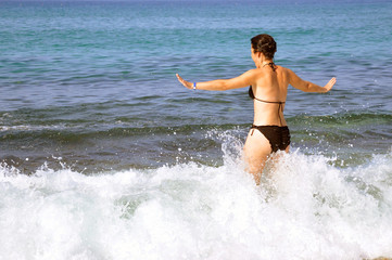 Young beautiful woman. A woman in a black swimsuit enjoys walking on the sea waves and takes sunbathing