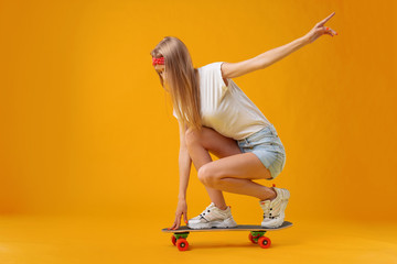 Skateborder girl in shorts and T-shirt sitting on board over yellow background © fotofabrika