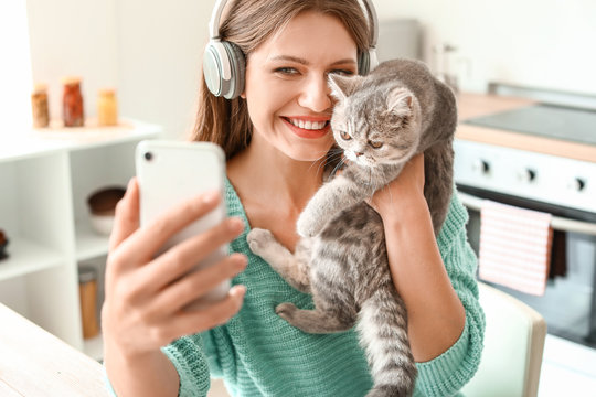 Beautiful young woman taking selfie with cute cat in kitchen