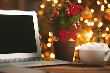 Wooden desk with computer with blank screen against blurred christmas lights background