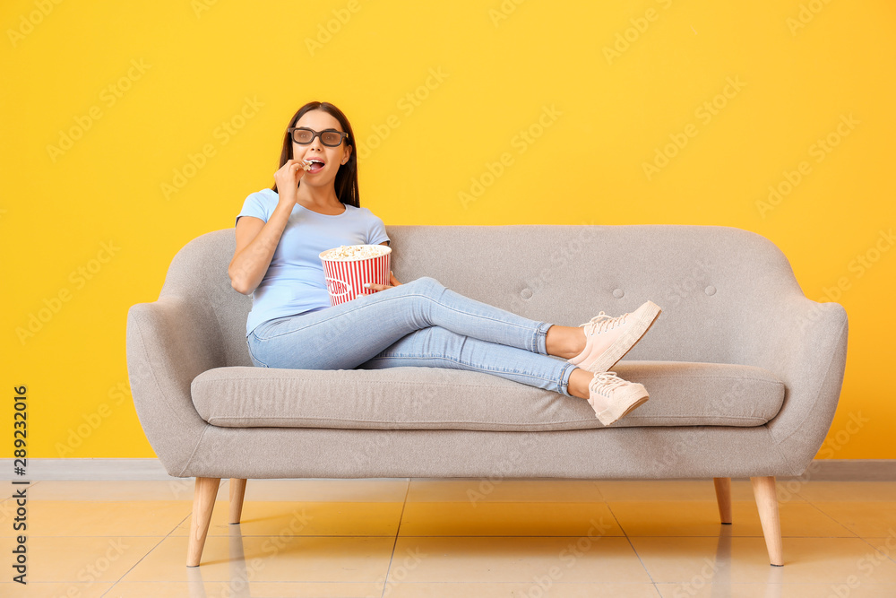 Canvas Prints Young woman with popcorn watching movie on sofa near color wall