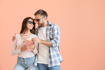 Young couple eating popcorn on color background