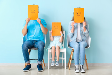 Young family hiding faces behind emoticons near color wall