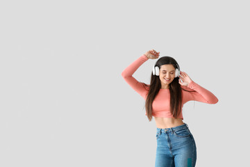 Beautiful young woman listening to music and dancing against light background