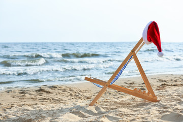 Fototapeta na wymiar Beach chair with Santa Claus hat on sea coast. Christmas vacation