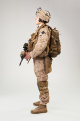 Soldier in US marines uniform with rifle on light grey background, studio shot
