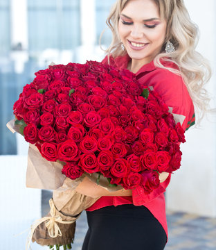 Elegant beautiful blonde woman is wearing green fashion dress in cafe holding with big bouquet of 101 red roses. Birthday.
