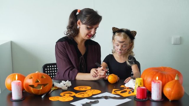 Young Mother and her Little Daughter Making Crafts for Halloween. They are Drawing Scary Face on a Tangerine. Holidays and Halloween Decorations Concept