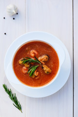 Tomato soup with seafood: shrimps and mussels on a white wooden table. Flat lay, vertical orientation.