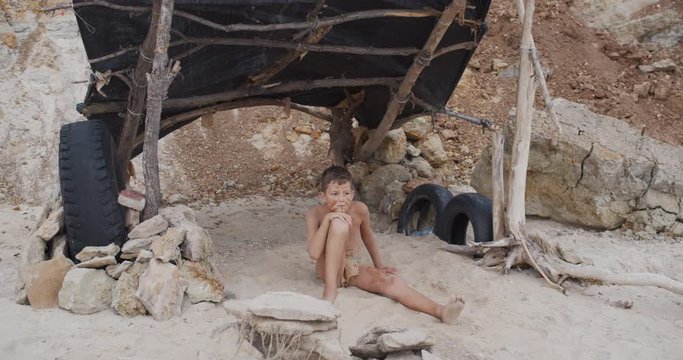 Caveman, manly boy. Funny young primitive boy outdoors. Evolution survival concept. Calm boy outside sitting at his rocky settlement. Prehistoric tribal man.