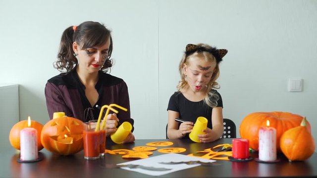 Young Woman with her Cute Daughter Making Crafts for Halloween from Orange Plastic Cups at Home. Holidays and Halloween Decorations Concept