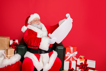 Portrait of his he nice cheerful kind generous fat bearded man St Nicholas reading address list clients wish want fairy miracle orders winter december isolated over bright vivid shine red background