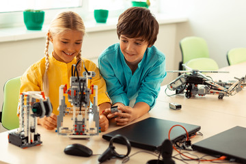 Boy helping his classmate turning on a robot.