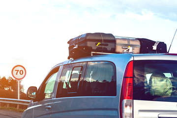 On the roof of a gray minivan, luggage - suitcases, goes along the highway, ahead of the sign -...
