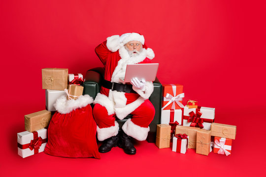 Full body photo of impressed santa claus in hat with eyewear eyeglasses read noel news on his laptop feel stupor isolated over red background