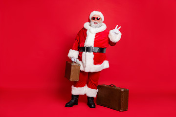 Full length body size view of nice attractive cheerful cheery fat bearded man carrying vintage heavy bag luggage baggage showing v-sign isolated on bright vivid shine red background